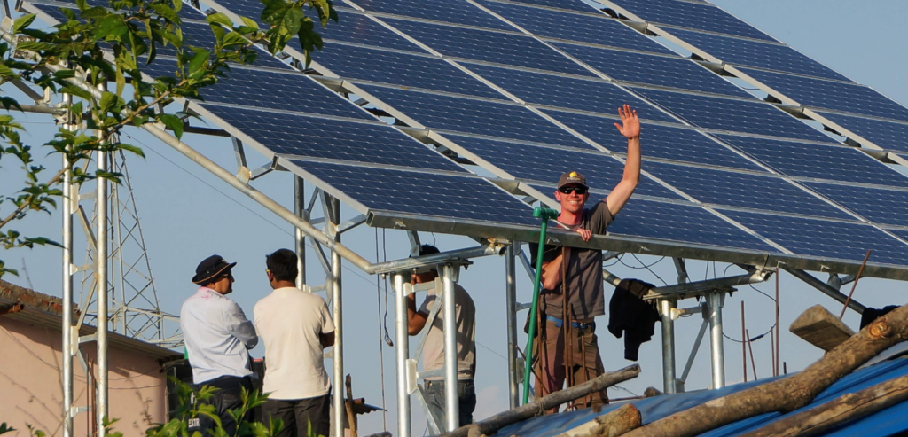 waving smiling man next to a solar pv system in nepal